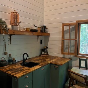 Eine kleine Küche mit einer Holzausziehtafel, einem Spülbecken und einem Fenster mit Blick auf Grünflächen.