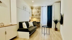 A modern living room with a sofa, a small side table, a flat-screen TV mounted on the wall, and a stone accent wall. - Cocon Lamartine (Niza)