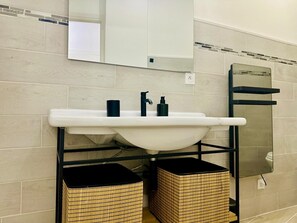 A bathroom with a white sink, black faucet, and a mirror above it. There are two wicker baskets under the sink. - Cocon Lamartine (Niza)