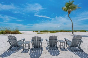A beach with four Adirondack chairs and a palm tree. - 🌊Beach Front with Great Views-Pool+Hot Tub-Pelican Watch #602🌊 (Fort Myers Beach)