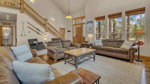 Un vaste salon doté d’un escalier en bois, de canapés en cuir, d’une table basse en bois et de grandes fenêtres offrant une vue sur l’extérieur.