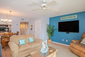 A living room with a beige sofa, a brown leather chair, a coffee table, a TV, and a sign that reads "BEACH HOUSE". - Seaside Cottage, water views, Fishing & Boat Pier! (Rockport)