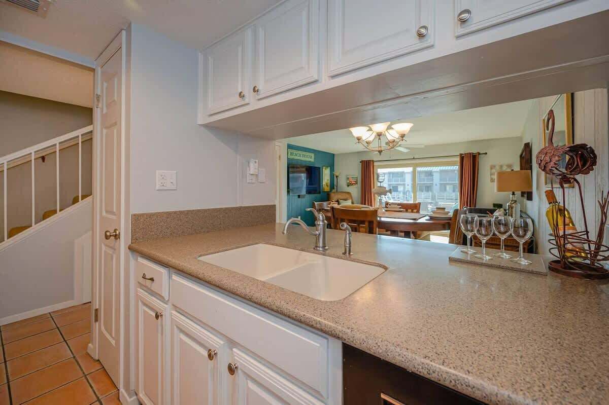 A kitchen with white cabinets, a granite countertop, and a sink. There is a dining area with a table and chairs visible through an open door.