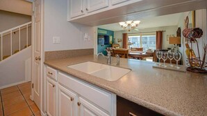 A kitchen with white cabinets, a granite countertop, and a sink. There is a dining area with a table and chairs visible through an open door.
