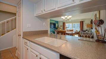 A kitchen with white cabinets, a granite countertop, and a sink. There is a dining area with a table and chairs visible through an open door.
