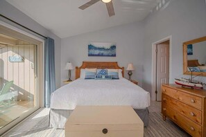 Une chambre à coucher comprenant un lit, un ventilateur de plafond, un tableau, une commode et une porte-fenêtre coulissante.