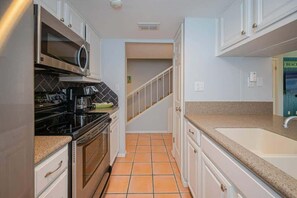 Una cocina con armarios blancos, un microondas de acero inoxidable, una estufa negra y una encimera color beige.