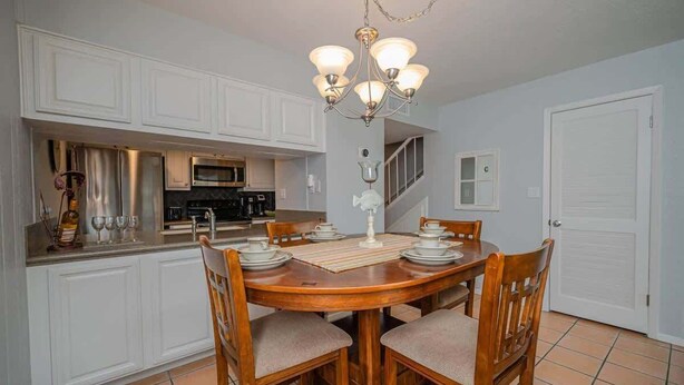 A dining area with a round wooden table, four chairs, a chandelier, and white cabinetry.