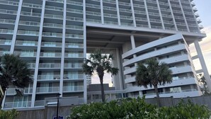 Un hôtel moderne à plusieurs étages, doté d’une série de balcons, d’une galerie couverte et de palmiers au premier plan.