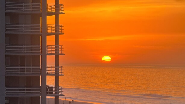 Un immeuble de grande hauteur doté de balcons donnant sur une plage au coucher du soleil.