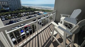 Un balcon avec des chaises blanches donnant sur un parking et une plage.