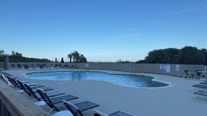 Une piscine entourée d’un mur bas, agrémentée de chaises longues et de tables, mais sans panneaux indiquant la présence d’un sauveteur.
