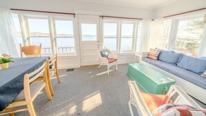 Ett rum med ett matbord, stolar, en soffa och utsikt över havet genom stora fönster.