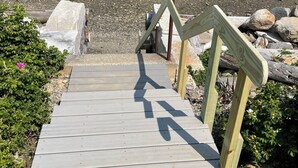 En träbrygga som leder fram till en stenstrand, med en båt synlig i bakgrunden.