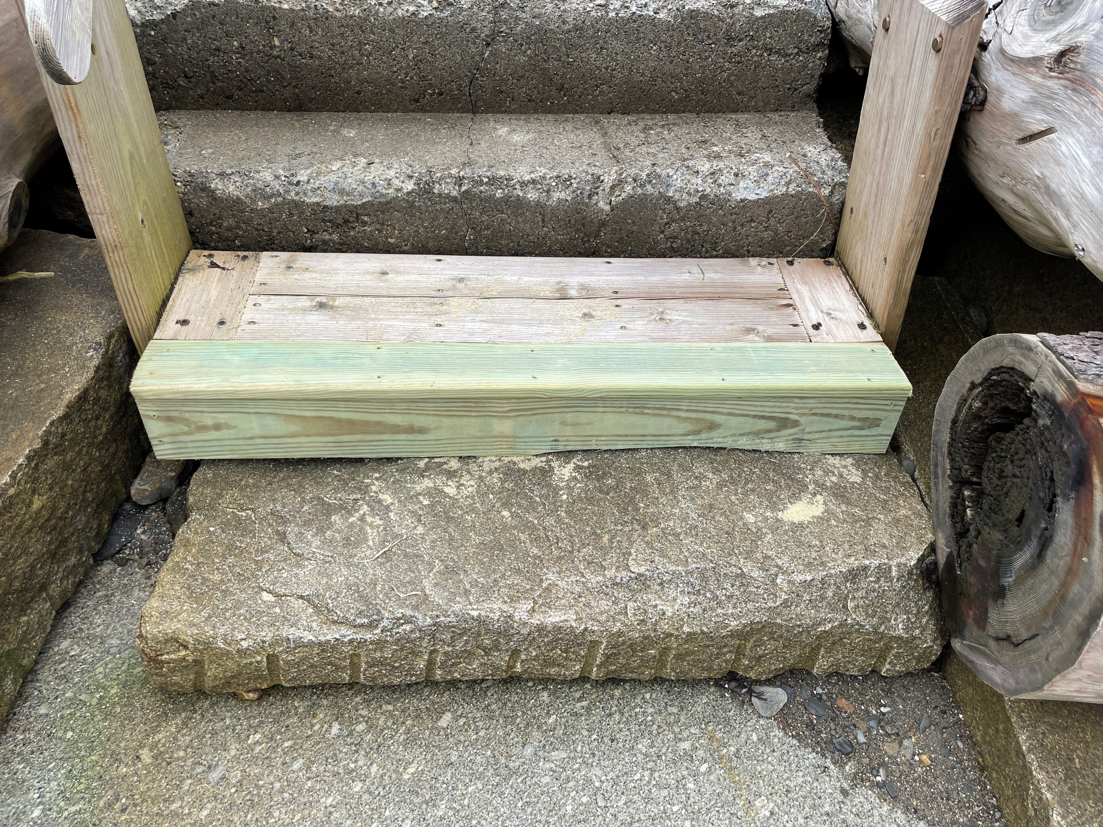 Un banc en bois doté d’une structure métallique, placé sur une marche en pierre.