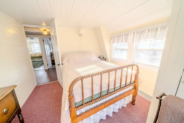 A bedroom with a wooden bed, a nightstand, a window with curtains, and a door leading to another room.
