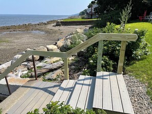 A wooden staircase leading to a beach area with a view of the ocean and a house in the background.