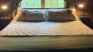 Una cama acogedora con un colcha estampada, dos lámparas de noche y una ventana con cortinas.