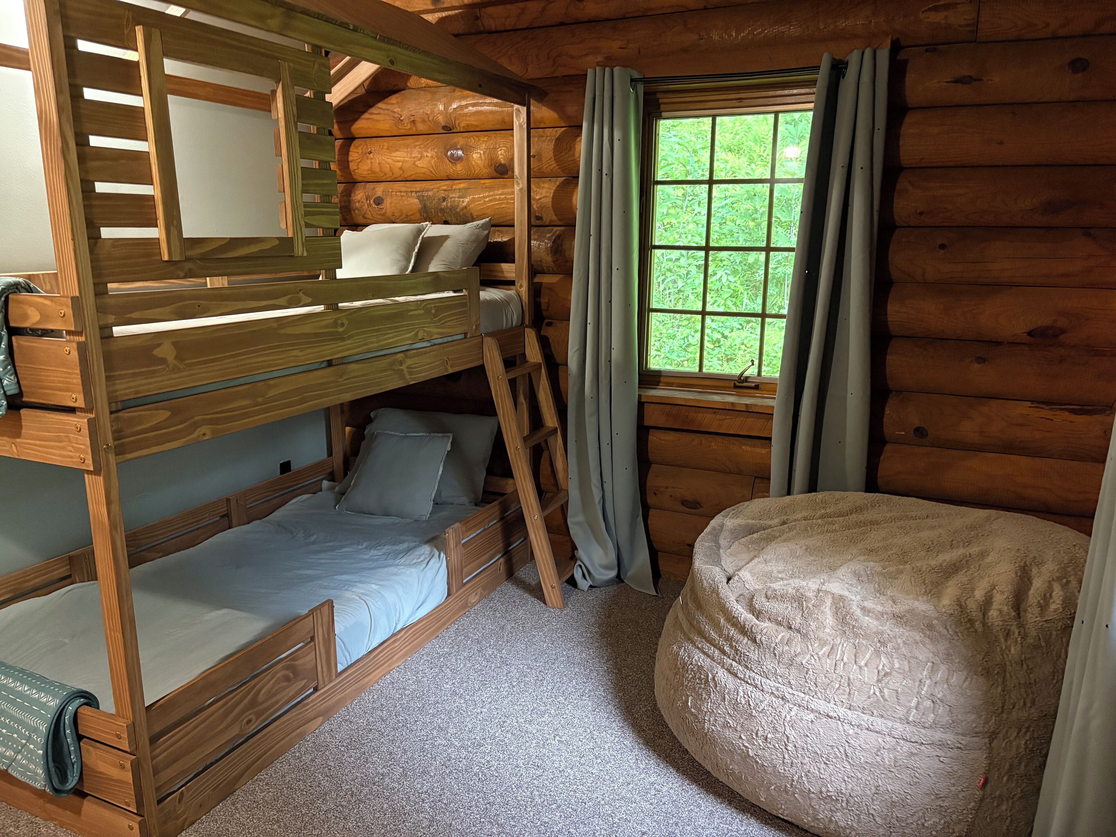 A wooden cabin room with bunk beds, a large round bean bag, and a window with curtains.