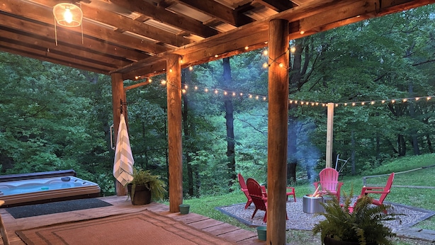 Una terraza de madera con un jacuzzi, sillas rojas y luces colgantes.