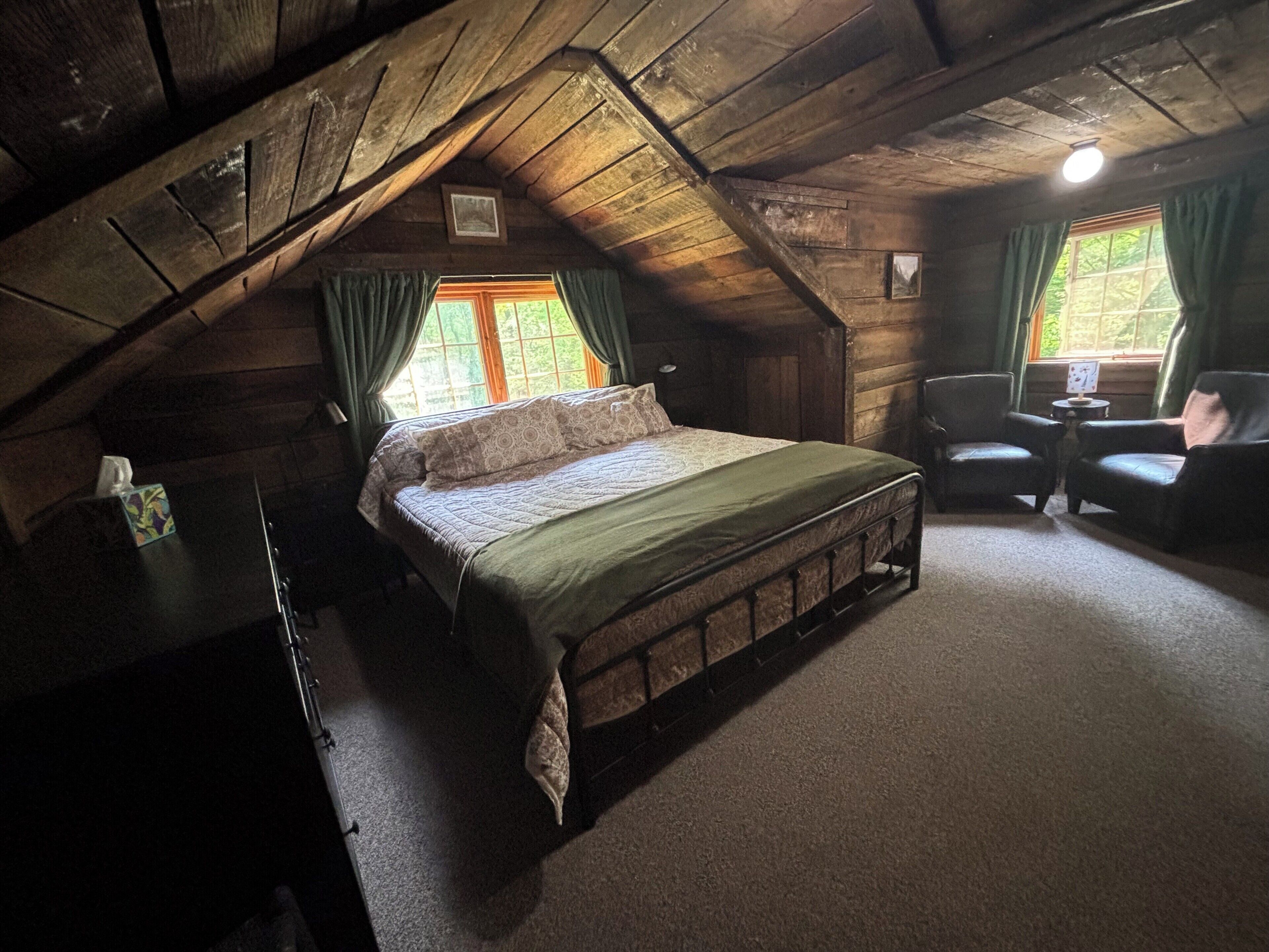 Ein gemütliches Schlafzimmer im Dachgeschoss mit schrägen Holzwänden, einem Einzelbett, zwei Stühlen und einem kleinen Tisch.
