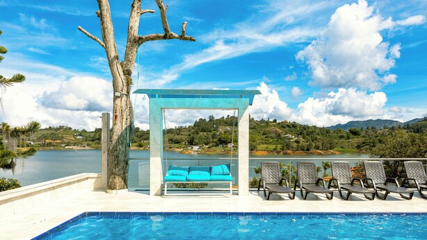 Une piscine avec un banc et des chaises, une pergola et une vue sur un lac et des collines.