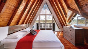 Une chambre avec un plafond en bois, un lit avec une literie blanche, un plaid rouge et une commode.