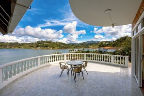A balcony with a table and chairs overlooking a lake and mountains.