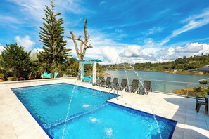 A swimming pool with a view of a lake and mountains, surrounded by lounge chairs and a waterfall feature.