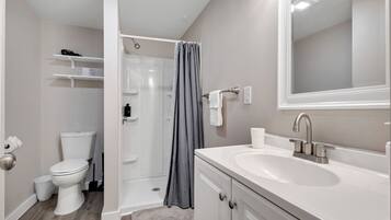 Une salle de bain moderne avec un lavabo blanc, des toilettes, une douche avec un rideau gris et un miroir au-dessus du lavabo.