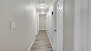 A narrow hallway with white walls and a wooden floor. There are white doors on the right and a light switch on the left. - Judkins Retreat - Close to Downtown (Seattle)