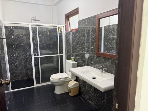 A bathroom with a shower, toilet, and sink, all with marble walls and black tiles.