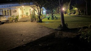 Un'area esterna ben illuminata con un vialetto lastricato, piante in vaso e un angolo relax con sedie.