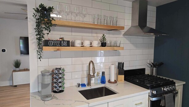A modern kitchen with white cabinetry, a built-in stove, and a coffee bar with mugs and a sign.