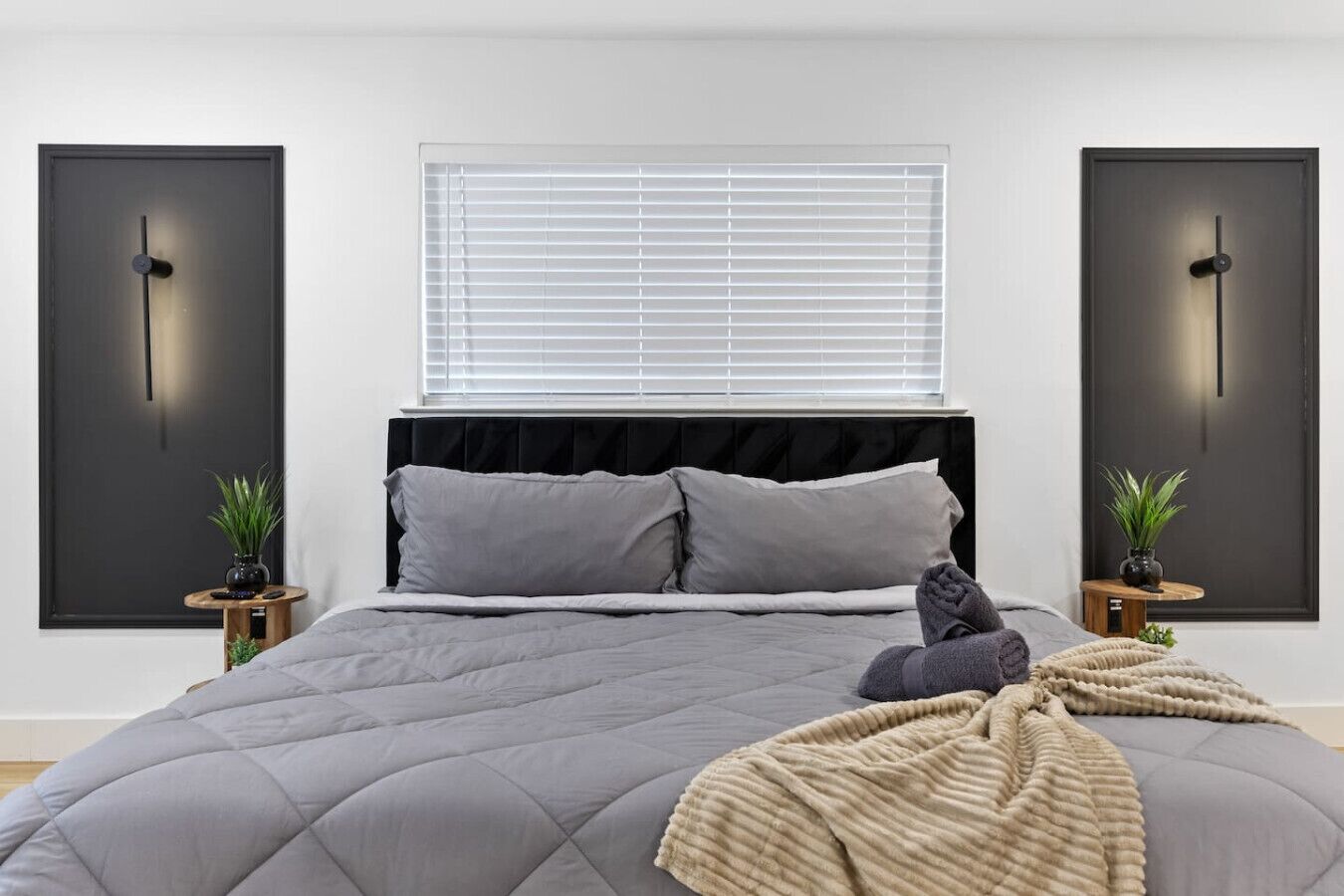 A modern bedroom with a large bed, a window with blinds, and two wall-mounted clocks.