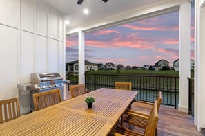 Eine überdachte Terrasse mit Holztisch und -stühlen, einem Grill und Blick auf Häuser über dem Wasser.