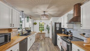 A modern kitchen with white cabinets, wooden countertops, a central island, and a stainless steel refrigerator.