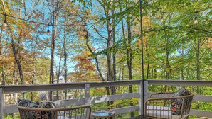 A wooden deck with wicker chairs and a small table, overlooking a forested area.