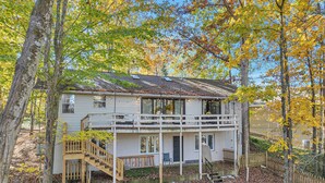 A two-story house with a balcony, surrounded by trees and covered in autumn leaves.