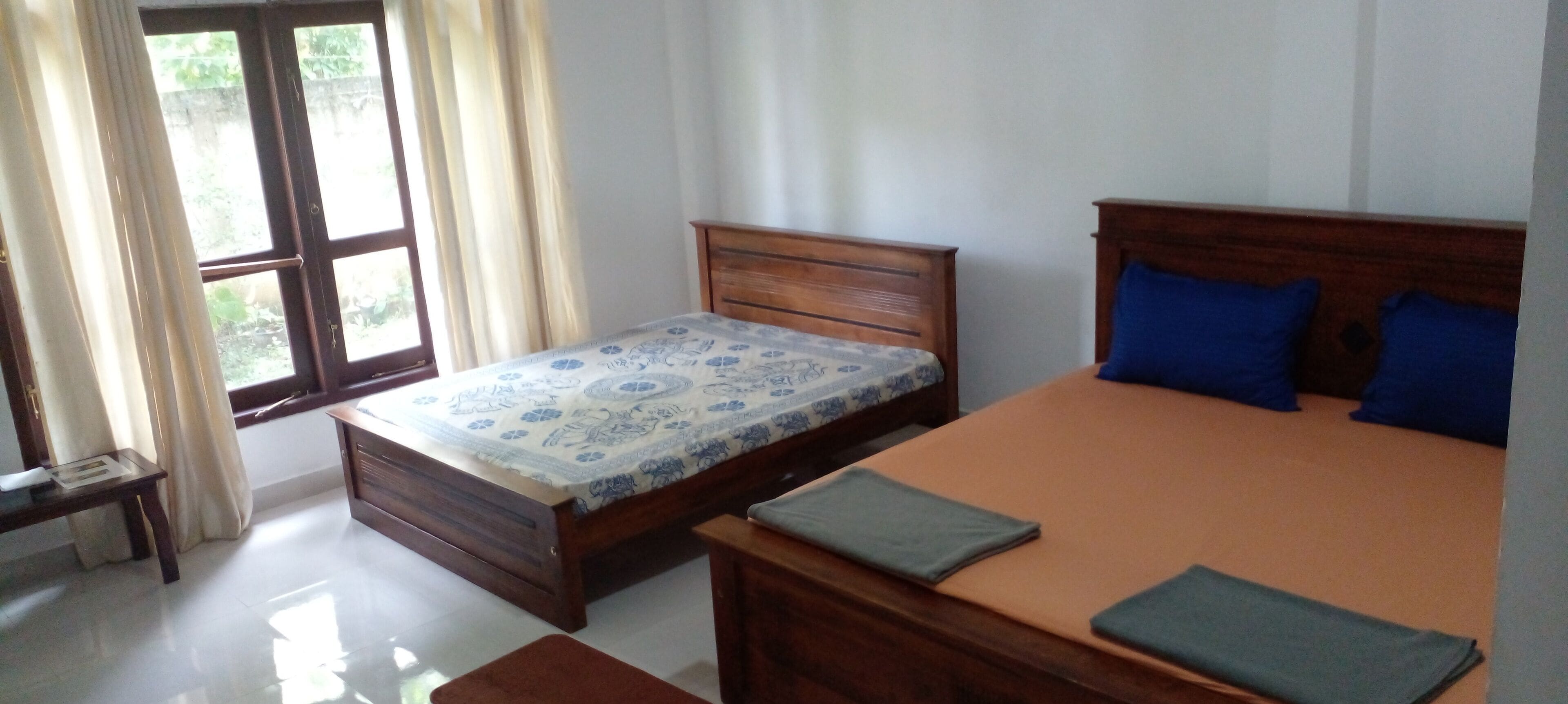 A bedroom with two beds, a wooden headboard, a window with curtains, and a small table.