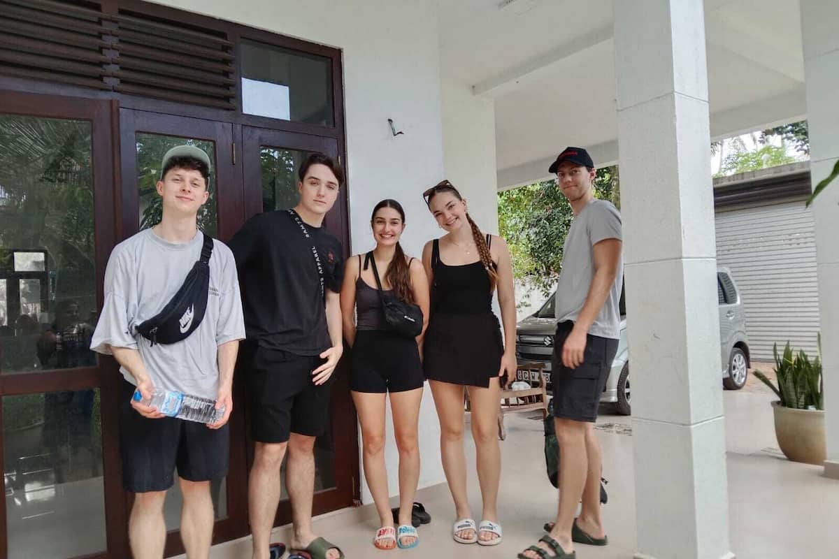 Un groupe de personnes se tient devant un bâtiment doté de grandes fenêtres, et une voiture est garée à proximité.