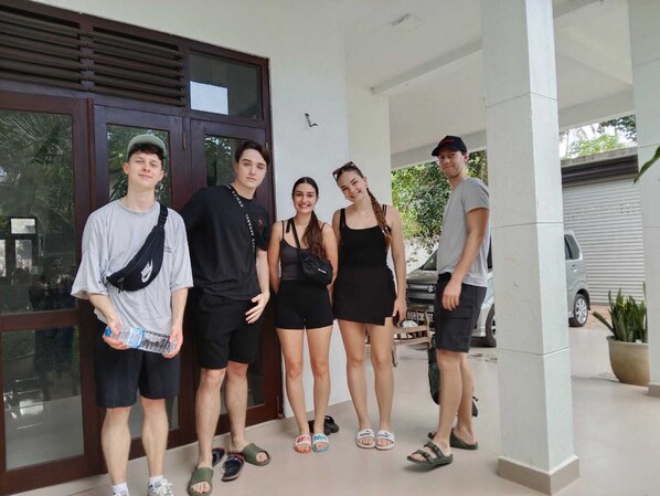 A group of people standing in front of a building with large windows and a car parked nearby. - Bosadi Homestay (katunayake)