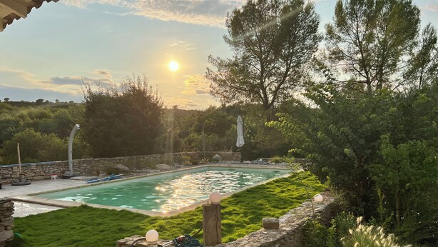 A swimming pool with a stone wall and grass in the foreground, surrounded by trees and a clear sky. - Family home with large pool and garden - Peace and quiet guaranteed (Aubais)