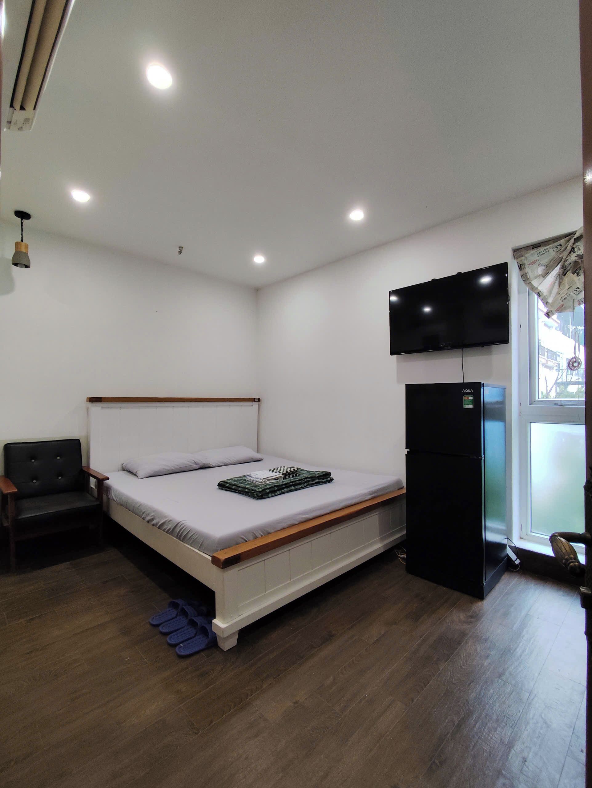 A bedroom with a bed, a black refrigerator, a television, and a window with curtains.