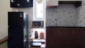 A kitchen with a black refrigerator, a microwave, and a sink. There is a window with a curtain, and the floor is wooden. - NAVILA homstay free laundry (Ho Chi Minh City)
