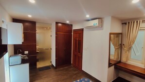 A compact hotel room with a wooden wardrobe, a small kitchenette, and a window with curtains. - NAVILA homstay free laundry (Ho Chi Minh City)
