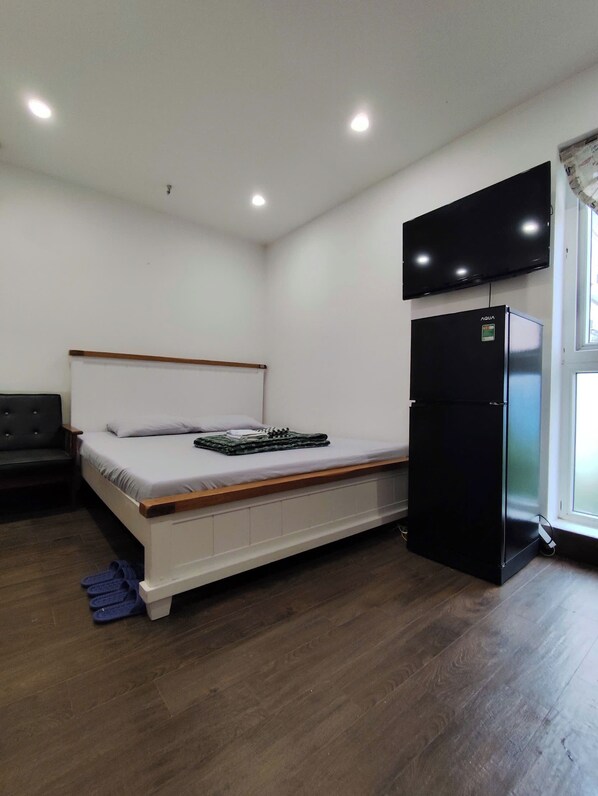 A bedroom with a bed, a black refrigerator, a television mounted on the wall, and a window.