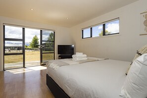 A bedroom with a bed, a TV, and a view of a grassy area through a sliding door.