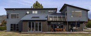A modern two-story house with a flat roof, large sliding glass doors, and a balcony with outdoor seating.