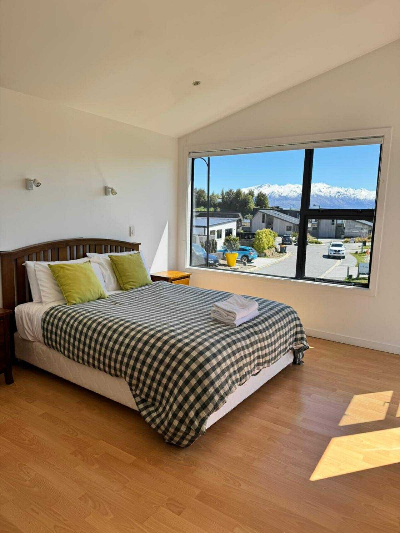 Een slaapkamer met een groot raam, een bed met geruit beddengoed en uitzicht op een besneeuwd berglandschap.